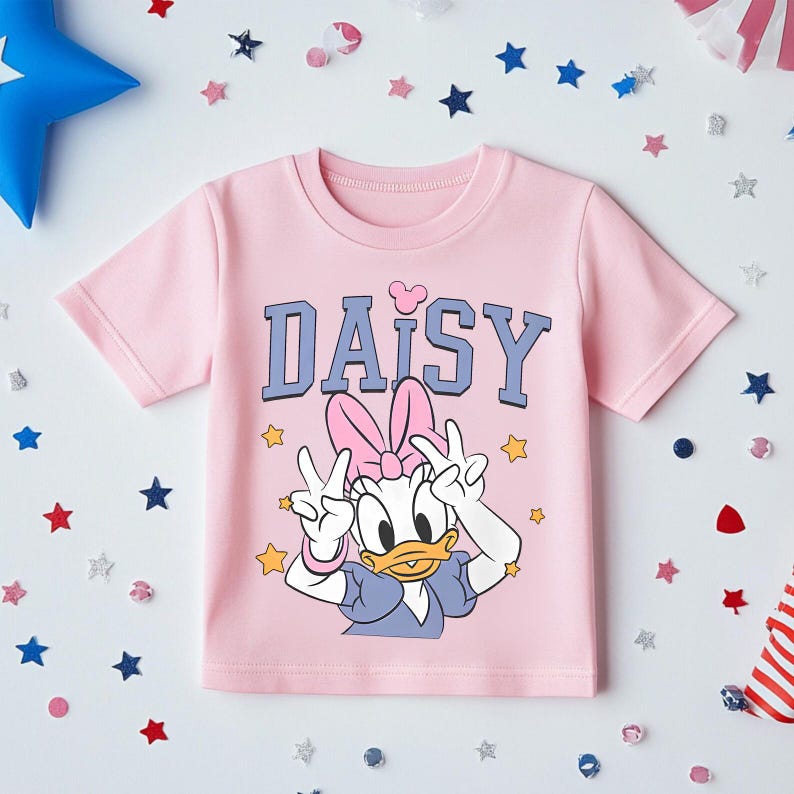 K&ouml;nnte beinhalten: Hellrosa T-Shirt mit dem Wort "DAISY" in blauen Buchstaben und einem Herz &uuml;ber dem "I". Das T-Shirt zeigt eine Grafik von Daisy Duck, die Friedenszeichen macht. Sternf&ouml;rmiges Konfetti umgibt das T-Shirt.