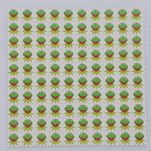 May include: A sheet of perforated paper featuring a repeating pattern of Kermit the Frog's face. Each frog has green skin, red lips, and large, round eyes. The background is a light beige color.