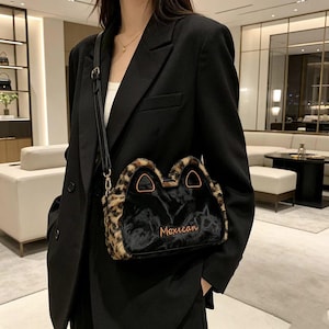 Puede incluir: Un bolso negro con una forma única y un ribete de estampado de leopardo. El bolso tiene un centro negro con la palabra "Mexican" en escritura naranja. Se lleva al hombro con una correa negra.