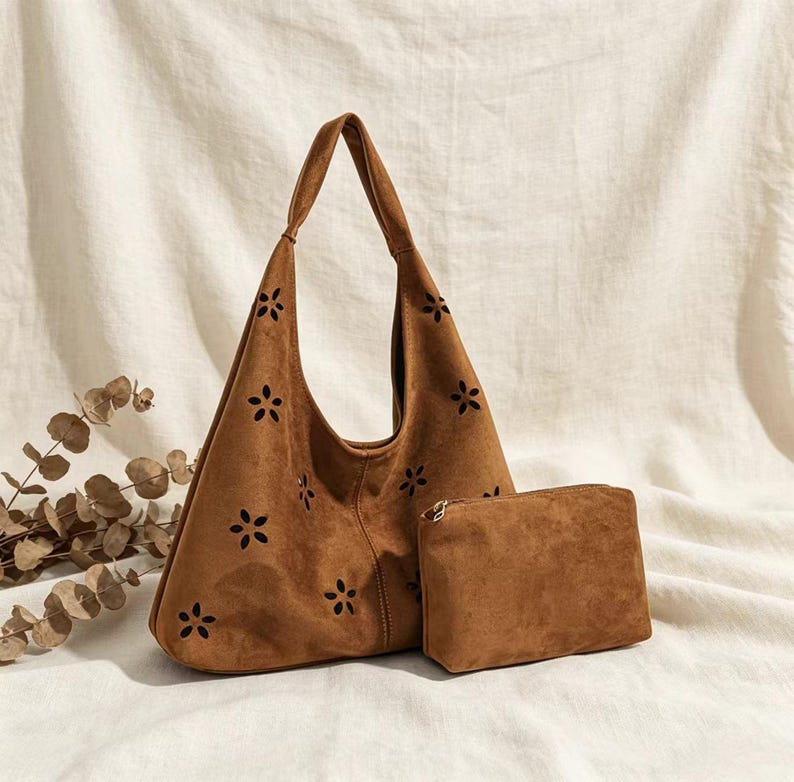 May include: A brown suede shoulder bag with a matching small pouch. The bag features a floral cut-out design and a single shoulder strap. The pouch has a zipper closure. The set is displayed on a white fabric background.