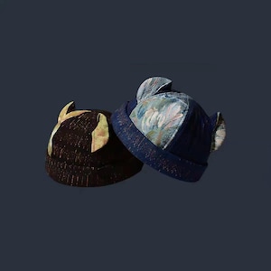 May include: Two hats with ear-like flaps. One is dark brown with gold accents, the other is navy blue with a floral pattern. Both hats have a rounded crown and a brim. The hats are made of a textured fabric.