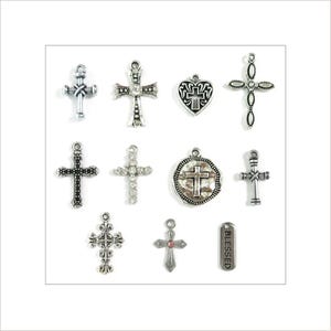 May include: A collection of silver-toned cross charms in various designs. Some crosses feature ornate detailing, while others have a simple, classic look. One charm is heart-shaped with a cross design, and another has the word "BLESSED" engraved.