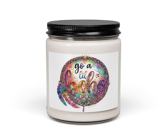 May include: A clear glass candle jar with a black lid containing white wax. The label features a circular, multicolored, intricate design with feathers and floral patterns, displaying the text "go a lil boho" in a stylized, cursive font.