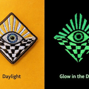 Puede incluir: Parche bordado con un diseño de ojo, rayos de sol y un patrón de tablero de ajedrez. El parche brilla en la oscuridad. El texto dice "Daylight" y "Glow in the Dark". El parche tiene forma de diamante.