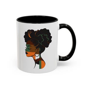 May include: White ceramic mug with a black interior and handle. The mug features a side profile illustration of a woman with dark skin and curly black hair. The design includes orange, green, and brown accents, and a gold hoop earring.