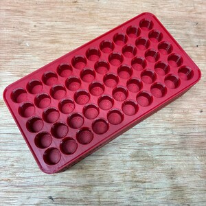 Pode incluir: Uma bandeja de armazenamento retangular de pl&aacute;stico vermelho com uma grade de cinquenta compartimentos circulares embutidos, dispostos em cinco fileiras de dez. A bandeja tem um acabamento liso e brilhante com uma estrutura uniforme.