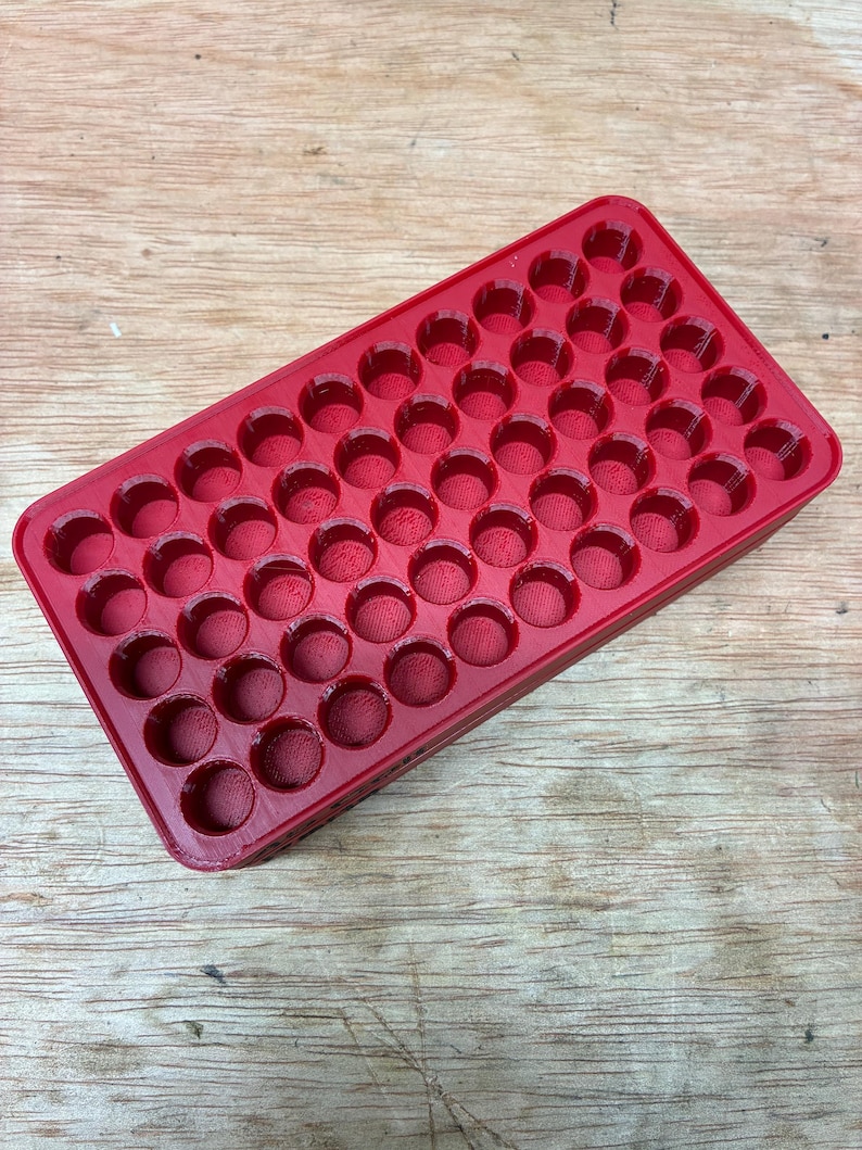 Pode incluir: Uma bandeja de armazenamento retangular de pl&aacute;stico vermelho com uma grade de cinquenta compartimentos circulares embutidos, dispostos em cinco fileiras de dez. A bandeja tem um acabamento liso e brilhante com uma estrutura uniforme.