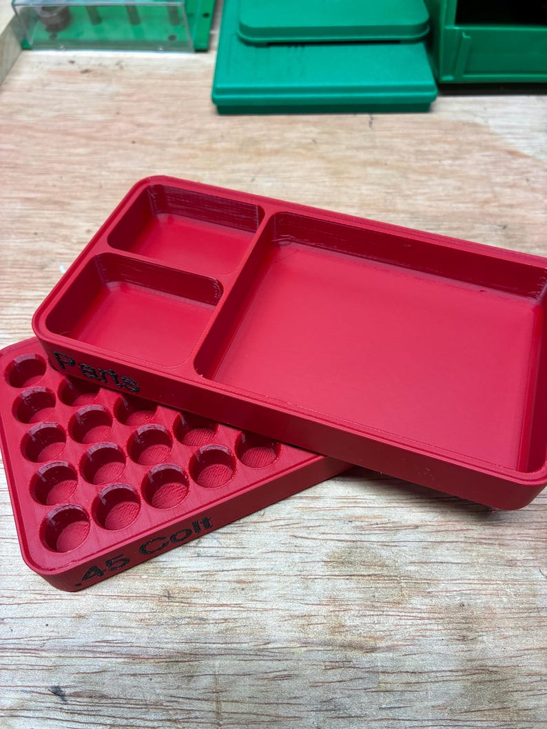 Pode incluir: Uma bandeja de armazenamento de pl&aacute;stico vermelho com v&aacute;rios compartimentos e uma bandeja vermelha separada com uma grade de orif&iacute;cios circulares. A lateral da bandeja tem o texto preto em relevo .45 Colt e a palavra Parts.