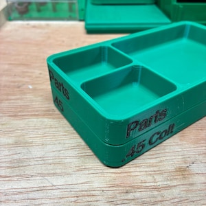 Pode incluir: Uma bandeja de armazenamento de pl&aacute;stico verde com tr&ecirc;s compartimentos distintos. A lateral da bandeja apresenta um texto impresso em preto que diz Parts e .45 Colt. A bandeja tem formato retangular com cantos arredondados e acabamento liso.