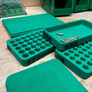 Pode incluir: Um conjunto de bandejas de recarga e caixas de armazenamento de pl&aacute;stico verde. Uma bandeja est&aacute; rotulada como 6.5 Creedmoor, outra como .223 e uma terceira como Bullets, contendo v&aacute;rios proj&eacute;teis met&aacute;licos de cor cobre.