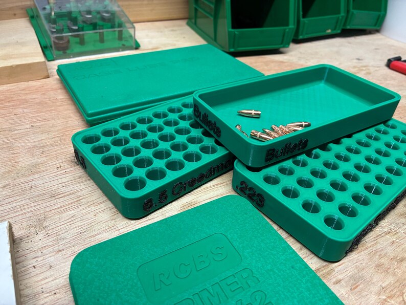 Pode incluir: Um conjunto de bandejas de recarga e caixas de armazenamento de pl&aacute;stico verde. Uma bandeja est&aacute; rotulada como 6.5 Creedmoor, outra como .223 e uma terceira como Bullets, contendo v&aacute;rios proj&eacute;teis met&aacute;licos de cor cobre.