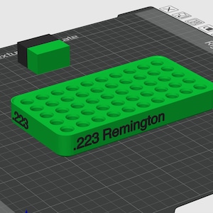 Pode incluir: Uma bandeja retangular de pl&aacute;stico verde para armazenamento de muni&ccedil;&atilde;o com uma grade de orif&iacute;cios circulares para cartuchos. A lateral da bandeja apresenta o texto impresso em preto .223 Remington. Um pequeno bloco retangular preto e verde est&aacute; posicionado atr&aacute;s.