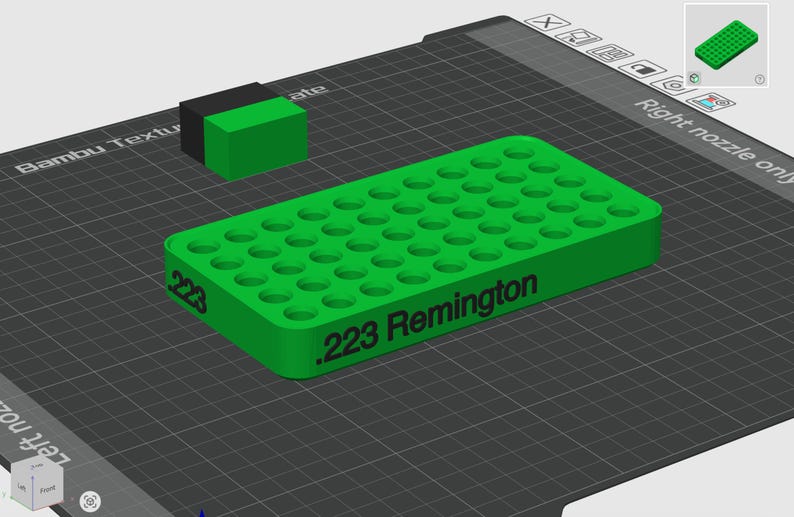 Pode incluir: Uma bandeja retangular de pl&aacute;stico verde para armazenamento de muni&ccedil;&atilde;o com uma grade de orif&iacute;cios circulares para cartuchos. A lateral da bandeja apresenta o texto impresso em preto .223 Remington. Um pequeno bloco retangular preto e verde est&aacute; posicionado atr&aacute;s.