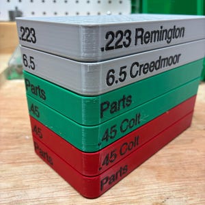 Pode incluir: Uma pilha de seis bandejas retangulares de pl&aacute;stico nas cores branca, verde e vermelha. As laterais possuem texto em preto, incluindo .223 Remington, 6.5 Creedmoor, .45 Colt e Parts. Cada bandeja apresenta um padr&atilde;o de grade no topo.
