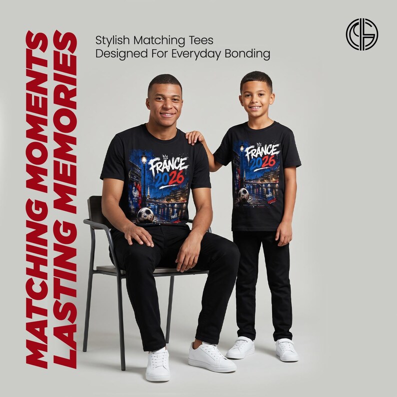 May include: Two black t-shirts featuring a graphic print of a night cityscape with the text "FRANCE 2026" in white, blue, and red. The design includes a soccer ball, a street lamp, and a bridge. The shirts are worn with black pants and white sneakers.