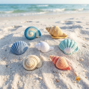 Puede incluir: Una colección de seis conchas marinas de ganchillo en varias formas y colores, incluyendo una espiral azul, un cono beige, un abanico azul, una pequeña espiral blanca, un abanico verde claro, una espiral crema y un cono color melocotón.