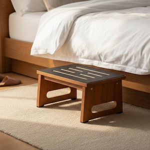 May include: A wooden step stool with a dark top and a natural wood finish. The stool has a rectangular shape with a slotted top and is placed on a beige rug near a bed. The stool measures approximately 16 inches long, 12 inches wide, and 10 inches high.