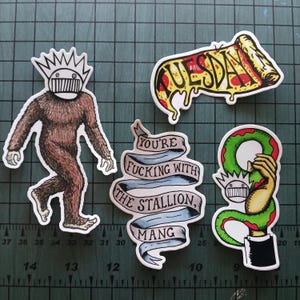 Puede incluir: Una colección de cinco pegatinas con varios diseños. Una presenta una criatura marrón y peluda. Otra muestra una porción de pizza con la palabra "TUESDAY". Una pancarta dice "YOU'RE FUCKING WITH THE STALLION, MANG".