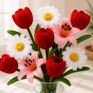 May include: A bouquet of handcrafted chenille flowers in a clear glass vase. The arrangement features deep red tulips, white daisies with yellow centers, and light pink lilies with dark brown stamens, all supported by green stems and leaves.