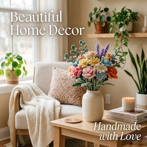 K&ouml;nnte beinhalten: Ein farbenfrohes, handgefertigtes Blumenarrangement in einer cremefarbenen Vase auf einem Holztisch. Die Blumen umfassen rosa Rosen, gelbe G&auml;nsebl&uuml;mchen und blaue Akzente. Der Text "Beautiful Home Decor" und "Handmade with Love" sind sichtbar.