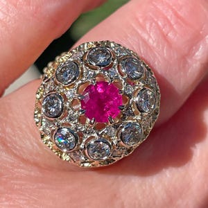 May include: A gold ring with a large pink ruby surrounded by smaller diamonds.