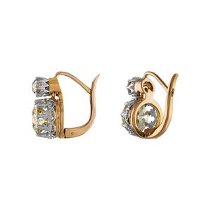 May include: A pair of gold-tone earrings with a lever back closure. Each earring features a light yellow gemstone and a smaller, clear gemstone. The gemstones are set in a silver-tone metal.