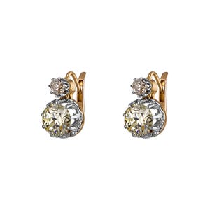 May include: A pair of antique gold and silver earrings. Each earring features a large, round, light yellow gemstone set in a silver and gold setting, with a smaller, round, light brown gemstone above it. The earrings have a lever back closure.