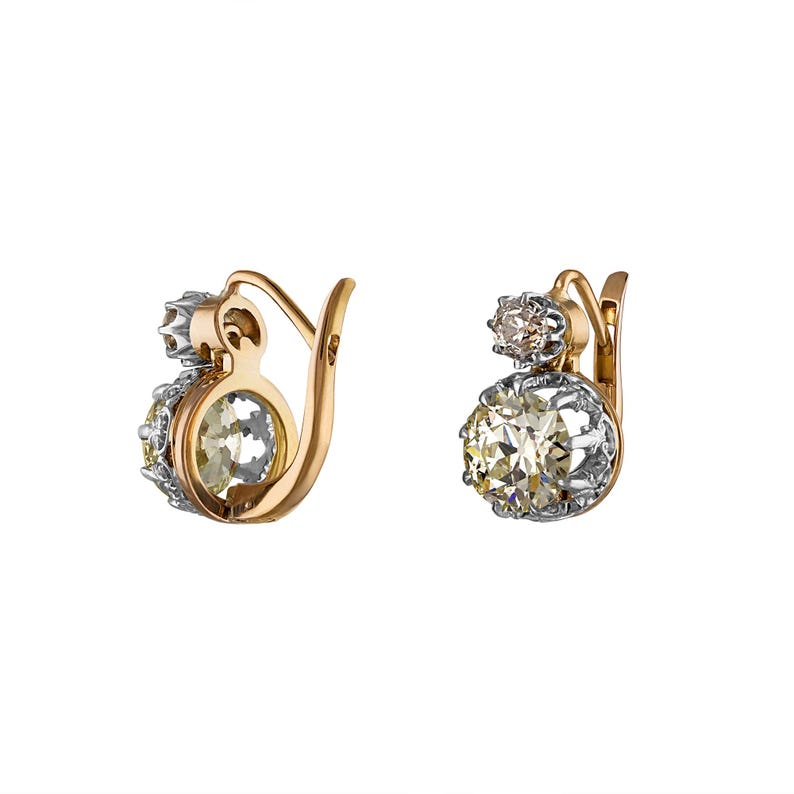 May include: A pair of gold and silver earrings with large, round, clear gemstones. The earrings have a hook closure and a smaller gemstone above the larger one. The gemstones are set in a silver and gold setting.