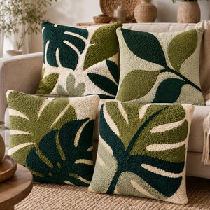 May include: Four square throw pillows featuring a textured, tufted surface with botanical leaf patterns in shades of dark green, olive green, and cream. The designs display various foliage shapes, including monstera leaves, arranged in a repeating pattern.