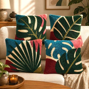 May include: A set of four square throw pillows featuring a textured punch needle design. Each pillow displays large, stylized tropical leaf patterns in deep green, cream, teal, and maroon, creating a vibrant and layered botanical aesthetic.