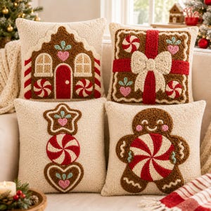 May include: Four square scatter cushions with cream-coloured textured fabric. Designs include a brown gingerbread house, a gift box with a red ribbon and bow, a vertical stack of a star, peppermint, and heart, and a smiling gingerbread person.