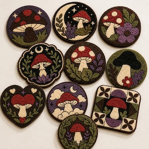 May include: A collection of ten punch needle coasters featuring various mushroom designs. The shapes include circles, a heart, and a square, with motifs of moons, stars, flowers, and foliage in colors of red, green, purple, black, and cream.