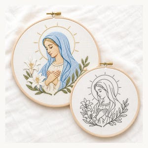 May include: Two circular wooden embroidery hoops containing fabric with stitched designs of a figure wearing a veil, surrounded by lilies and a halo. One design is fully colored in blue and cream tones, while the other is a black line art outline.