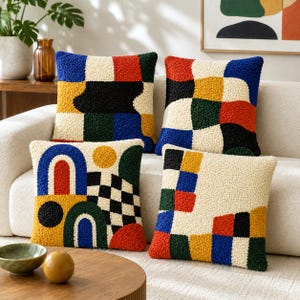 May include: Four square throw pillows featuring a textured, tufted surface with geometric patterns in cream, black, blue, red, yellow, and dark green. The designs include blocks, arches, circles, and checkerboard motifs across the four cushions.