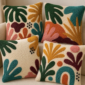 May include: Four square throw pillows with a cream-colored base featuring raised, textured tufted patterns in various shapes. The designs include abstract botanical and geometric motifs in shades of dark green, teal, mustard yellow, orange, pink, and deep maroon.