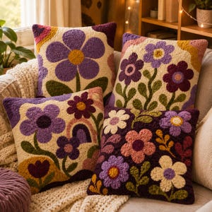 Peut inclure: Quatre coussins carrés ornés de broderies en punch needle texturées à motifs floraux. Les designs présentent de grandes fleurs violettes, roses et crème, des tiges vertes et des formes arquées dans des tons moutarde, bordeaux et lavande sur fond crème.