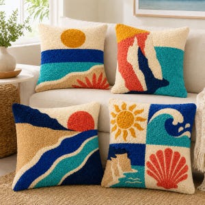 May include: Four square throw pillows with textured tufted designs featuring coastal and sun motifs. The patterns include a yellow sun over blue waves, abstract geometric shapes in red and blue, a sunset over sand dunes, and a sun, wave, and shell.