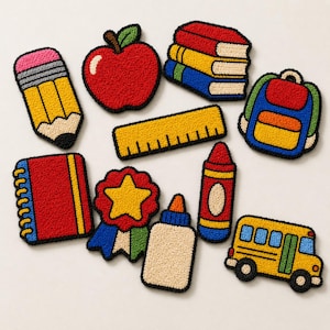 Peut inclure: Un ensemble d'écussons en punch needle sur le thème de l'école comprenant un crayon jaune, une pomme rouge, une pile de livres, un sac à dos bleu, une règle jaune, un carnet rouge, une étoile, de la colle, un crayon rouge et un bus scolaire.
