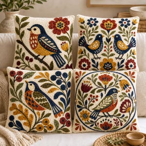 May include: Four square throw cushions featuring textured punch needle embroidery. Each cushion displays a cream background with colourful motifs of birds, flowers, leaves, and berries in shades of navy blue, mustard yellow, and deep red.