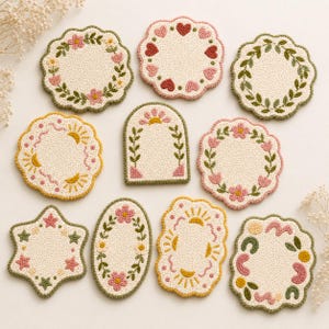 May include: A set of ten off-white, textured coasters with embroidered floral and geometric patterns. Each coaster has a scalloped edge and is decorated with pink, green, and yellow details. The shapes include circles, ovals, and a star.