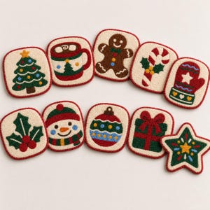 Könnte beinhalten: Ein Set aus zehn Punch-Needle-Untersetzern mit verschiedenen weihnachtlichen Motiven, darunter ein Weihnachtsbaum, ein Becher Kakao, ein Lebkuchenmann, eine Zuckerstange, ein Fäustling, Stechpalmenblätter, ein Schneemann, eine Christbaumkugel, ein Geschenk und ein Stern.