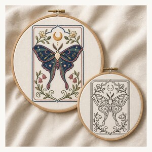 May include: Two circular wooden embroidery hoops containing fabric with moth designs. The larger hoop features a colorful embroidered moth with blue, green, and pink wings, a gold crescent moon, and floral accents. The smaller hoop shows a black line art version.