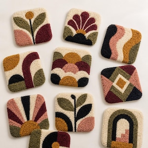 May include: A collection of ten square tufted coasters featuring various geometric and botanical patterns in a palette of cream, olive green, mustard yellow, deep burgundy, black, and dusty pink, each with a textured, raised loop pile surface.