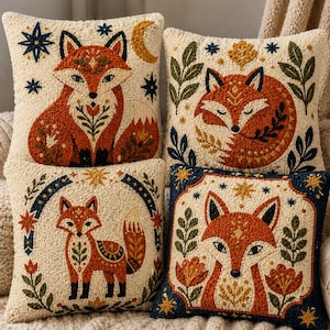 May include: Four square throw pillows featuring textured punch needle embroidery of foxes in orange, cream, and navy blue. Each pillow displays a unique fox illustration surrounded by botanical elements, stars, and crescent moon motifs on a cream background.