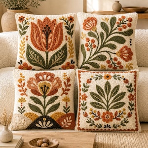 Peut inclure: Quatre coussins carrés avec une base couleur crème et une broderie à l'aiguille perforée texturée. Chaque coussin présente des motifs floraux et botaniques distincts dans des tons orange brûlé, jaune moutarde et vert forêt.