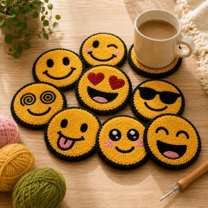 May include: A collection of yellow emoji-themed coasters with black borders, each featuring a different expression. A mug of coffee sits on one coaster. Yarn and a punch needle are also visible.