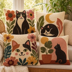 Peut inclure: Quatre coussins carrés présentant des motifs en punch needle texturé de chats et d'éléments botaniques. Les motifs incluent un chat noir et blanc assis avec des fleurs, un chat endormi avec un croissant de lune, un visage de chat calico et un chat noir avec une plante.