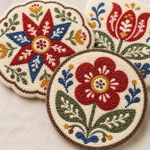 May include: Three round punch needle coasters featuring textured floral and star patterns in red, blue, green, and yellow yarn on an off-white background. The designs include a central star, a large red flower, and a tulip motif with intricate stitching.