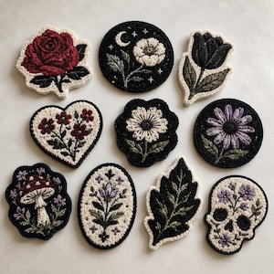 Könnte beinhalten: Eine Sammlung gestickter Aufnäher mit verschiedenen Designs. Enthält eine rote Rose, ein Herz mit Blumen, einen Pilz, einen Totenkopf, ein Blatt sowie florale und himmlische Motive. Die Aufnäher haben einen schwarzen Hintergrund mit cremefarbenen und farbigen Details.