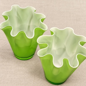May include: Two glass vases with a vibrant lime green exterior and a smooth white interior. Each vase features a distinctively ruffled, wavy rim that creates a flower-like opening, with a clear glass base visible at the bottom of each vessel.